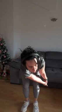 Kulaklık takan odaklanmış bir kadın oturma odasında spor yapıyor.