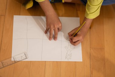 Boş kağıda dizilmiş bir ızgarada çizgi film karakteri çizen çocuk elleri