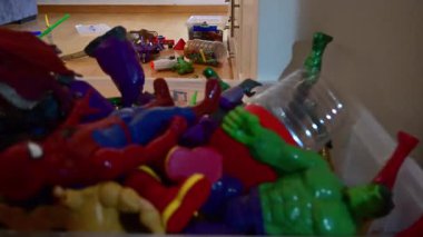 Çocuk dinazorlarla, araba izleriyle ve evdeki ahşap zemine saçılmış süper kahramanlarla mutlu bir şekilde oynuyor.