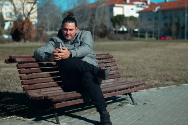 Parktaki bankta rahatlayan, akıllı telefonuyla meşgul olan bir adam.