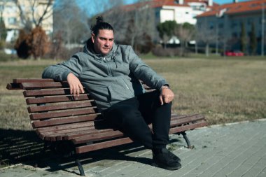 Yeşil çimenler ve konut binalarıyla çevrili bir bankta dinlenen bir adam.