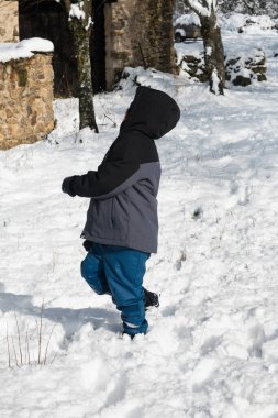 Küçük çocuk kış ceketi giymiş, taze karda oynuyor ve yürüyor.