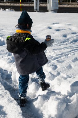 Küçük sıcak bir içecek konteynırını tutarken karlı bir arazide gezinen çocuk