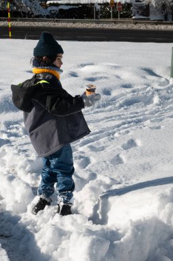 Kalın giysiler giymiş bir çocuk derin karda elinde ılık bir içecek bardağıyla ayakta duruyor.