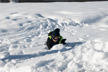 Sıcak kış giysileri giyen çocuk karla kaplı bir tarlada oynuyor.
