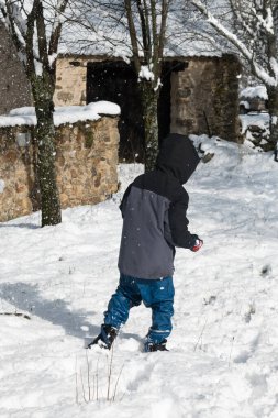 Kırsal bir kış sahnesinde taze karda yürüyen bir çocuk.
