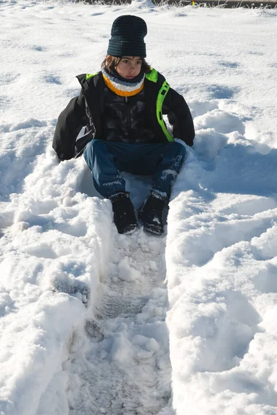 Kışın giyinmiş bir çocuk açık havada karlı bir günün tadını çıkarıyor.