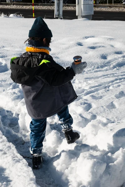 Küçük sıcak bir içecek konteynırını tutarken karlı bir arazide gezinen çocuk