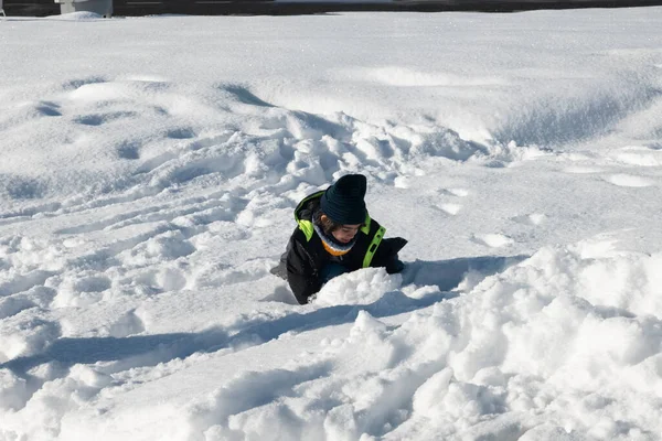 Sıcak kış giysileri giyen çocuk karla kaplı bir tarlada oynuyor.