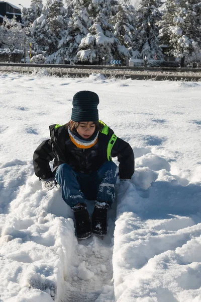 Taze karda oturan çocuk kış eğlencesinin tadını çıkarıyor.