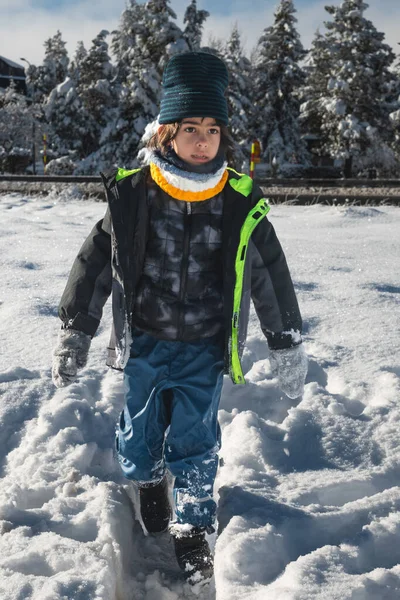 Kışın giysili bir çocuk açık havada taze beyaz bir karla oynuyor.