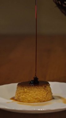 Tatlı karamel sosu yavaşça tatlı bir karamelli tatlıyı beyaz tabağa döküyor.