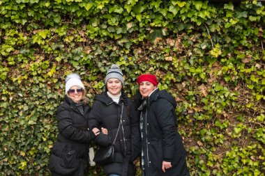 Bir grup gülümseyen kadın sarmaşık kaplı duvarın önünde yan yana duruyorlar.