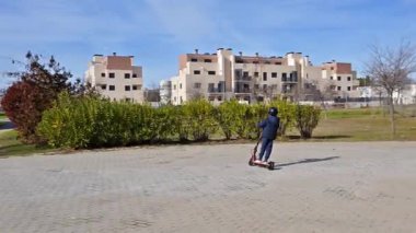 Kask takan genç bir çocuk, şehir parkında elektrikli scooterını sürerken eğleniyor.