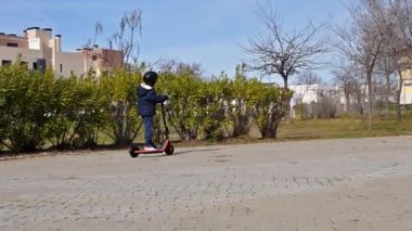 Küçük çocuk şehir parkında e-scooterıyla güneşli bir günün tadını çıkarıyor.