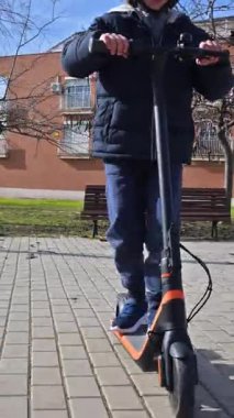 Kask takan genç bir çocuk parkta modern elektrikli scooterını sürerken eğleniyor.