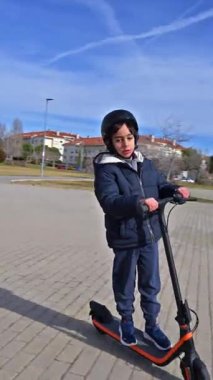 Çocuk şehir ulaşımı için çevre dostu elektrikli scooter kullanırken güneşli bir günün tadını çıkarıyor.