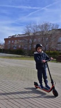 Koruyucu kask takan küçük bir çocuk güneşli bir günde açık havada elektrikli scooter sürmekten zevk alır.