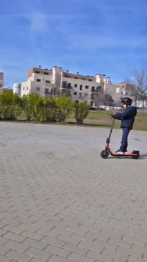 Kasklı bir çocuk, modern e-scooterını dışarıda asfalt bir yolda sürerken eğleniyor.