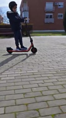 Genç bir çocuk şehirde güneşli bir günde elektrikli scooterıyla eğleniyor.
