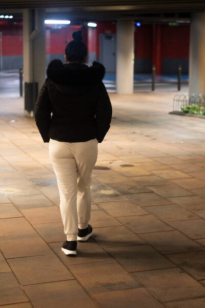 Woman in casual wear walking away from camera in a dimly lit parking garage at night