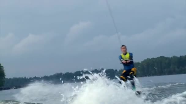 Hombre asiático wakeboarding detrás de un barco, salpicaduras de agua — Vídeos de Stock