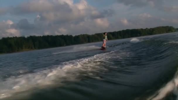 Mädchen auf dem Wakeborad springt die Welle hinter einem Boot, Sonnenuntergang — Stockvideo