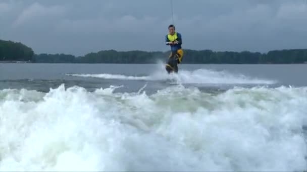 Wakeboarder uomo in tuta subacquea salta la scia dietro una barca a motore — Video Stock