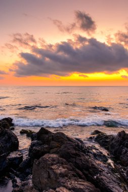 Yazın denizde gün doğumu. Sahilde, ufukta sıcak bir sabah gökyüzü parıltısıyla. Sakin deniz manzaralı sakin dalgalar tatil için arka planda. Bulutların arkasındaki güneş