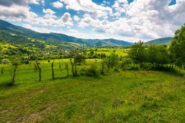 Yazın Ukrayna 'nın yuvarlanan tepelerindeki kırsal alanlar. Transcarpathia 'nın geniş açılı kırsal manzarası ve noktalı ışıkta çit var. Vadinin aşağısındaki Uzhok köyü. Karpatlar 'da yavaş yaşamak