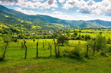 Yazın Ukrayna 'nın yuvarlanan tepelerindeki kırsal alanlar. Transcarpathia 'nın geniş açılı kırsal manzarası ve noktalı ışıkta çit var. Vadinin aşağısındaki Uzhok köyü. Karpatlar 'da yavaş yaşamak