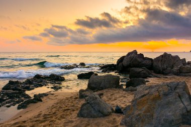 Şafak vakti kumlu ve taşlı Avrupa sahili. Bulgaria 'nın sabah güneşindeki güzel deniz manzarası. Romantik turuncu ışıltılı tatil geçmişi. Bulutlu dramatik gökyüzü