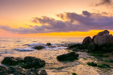 Şafak vakti kumlu ve taşlı Avrupa sahili. Bulgaria 'nın sabah güneşindeki güzel deniz manzarası. Romantik turuncu ışıltılı tatil geçmişi. Bulutlu dramatik gökyüzü