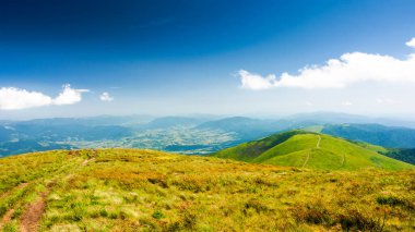 Yazın yeşil çayırları olan dağlık dağ manzarası. Güneşli bir günde uzak vadinin manzarası. Mavi gökyüzünün altındaki yuvarlanan tepelerde yemyeşil çimlerin olduğu güzel bir manzara. Ukrayna 'nın Karpat Alpleri