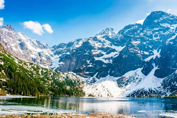 Tatra Ulusal Parkı 'ndaki Dağ Gölü. Morskie Oko ilkbaharın başlarında engebeli kar tepeleriyle çevriliydi. Su üzerindeki yansıma ve buzun güzel manzarası. yeşil arkaplan mavi gökyüzünün altında