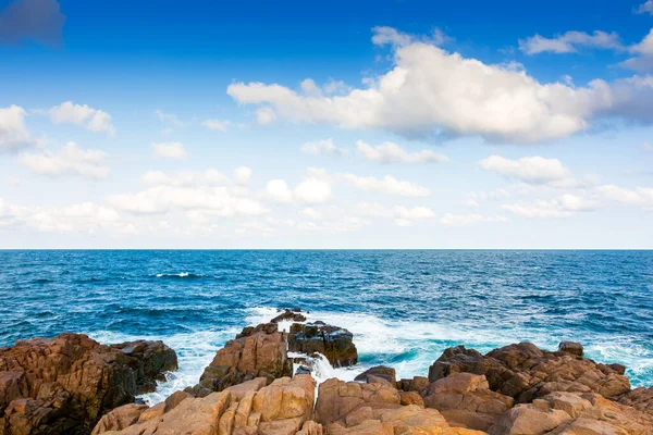 Güneşli bir akşamda dalgalar kayalık plajı vuruyor. Mavi gökyüzü ve öğleden sonra aydınlığında kabarık bulutlarla güzel bir sahil arkaplanı. İspanya 'nın deniz kıyısında bir seyahat yeri. Eğlence konsepti