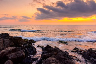 Yazın denizde gün doğumu. Sahilde, ufukta sıcak bir sabah gökyüzü parıltısıyla. Sakin deniz manzaralı sakin dalgalar tatil için arka planda. Bulutların arkasındaki güneş