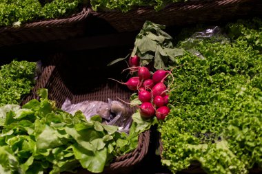 Turplar ve yeşil kıvırcık marul, sağlıklı gıda, taze ürün ve vejetaryen seçenekleri temsil eden bir markette dokuma sepetlerde sergileniyor.