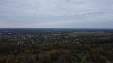 Sonbaharda ormandaki küçük bir köyün sonbahar manzarasının insansız hava aracı görüntüsü. Ormanın güzel sonbahar renkleri. Letonya 'nın sonbaharı