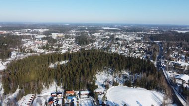 Kış mevsiminde karla ve ağaçlarla kaplı ormanlık bir kış şehri manzarası.