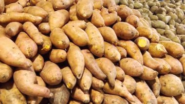 Taze patates ve tatlı patatesler süpermarkette üst üste dizilmiş.