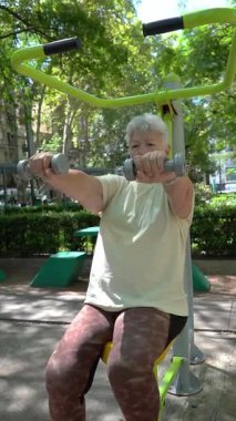 Kıdemli kadın yaz boyunca parkta ağırlık antrenmanı yapıyor.