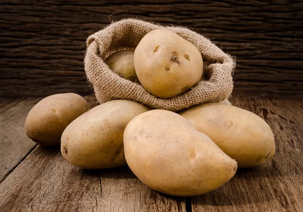 Fresh potatoes in hemp sack bags on rustic wooden background. — Stock Photo, Image