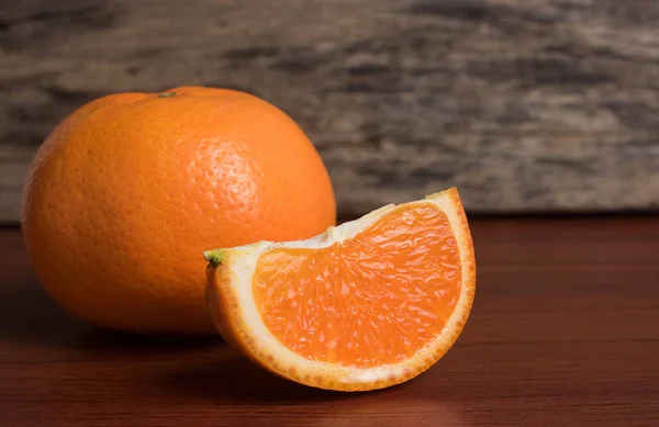 Fresh orange slice and whole orange on wooden table. Oranges are an excellent source of fiber and vitamin C. Antioxidants in oranges help protect skin from free radical damage and stop premature aging.