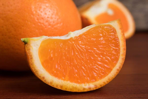 Fresh orange slice and whole orange on wooden table. Oranges are an excellent source of fiber and vitamin C. Antioxidants in oranges help protect skin from free radical damage and stop premature aging.