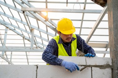 İnşaat işçisi inşaat halindeki evin duvarına köpük beton tuğlalar yerleştiriyor, ev inşa ediyor..