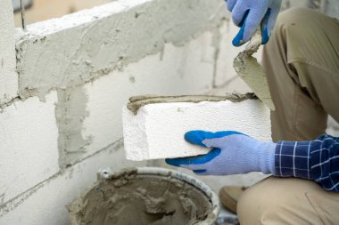 İnşaat işçisi inşaat halindeki evin duvarına köpük beton tuğlalar yerleştiriyor, ev inşa ediyor..