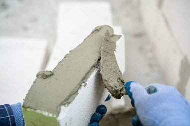 İnşaat işçisi inşaat halindeki evin duvarına köpük beton tuğlalar yerleştiriyor, ev inşa ediyor..