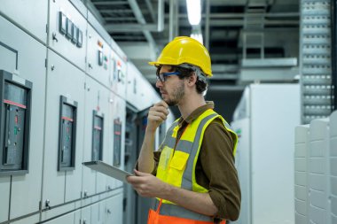 Mühendis, büyük sanayi fabrikasındaki modern bir termik santralin şanzıman odasında bir tablet bilgisayarı üzerinde çalışıyor..