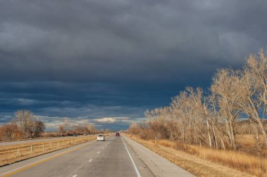 Otobanın üzerindeki güzel koyu mavi gökyüzü. Alışılmadık bir gökyüzü, yapraksız ağaçlar ve fırtınadan önceki bir sonbahar gününde asfalt bir yol. Pacific Junction, IA, ABD, 11-30-2019